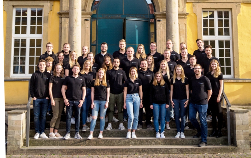 Gruppenfoto der Mitglieder der Fachschaft Wirtschaftswissenschaften (fachschaft|wiwi) aus dem Jahr 2018 auf den Treppen des Haupteingangs vom Schloss Osnabrück. Alle 34 Personen tragen ein schwarzes Polo-Shirt mit dem Logo der Fachschaft bzw. einen schwarzen Hoodie. Gruppenfoto der Mitglieder der Fachschaft Wirtschaftswissenschaften (fachschaft|wiwi) aus dem Jahr 2018 auf den Treppen des Haupteingangs vom Schloss Osnabrück. Alle 34 Personen tragen ein schwarzes Polo-Shirt mit dem Logo der Fachschaft bzw. einen schwarzen Hoodie.
